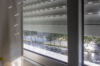 Pencereyi panjurlarla kaplayan yağmur damlaları Lizbon 'da bir sokak manzarası gösteriyor.