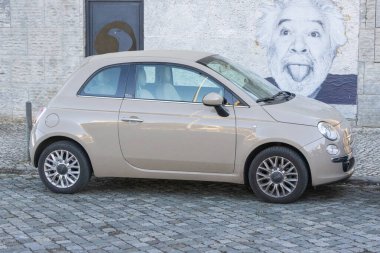 Fiat 500 üstü açık araba kaldırım taşlı bir caddeye park edilmiş, komik bir sokak resmi olan.