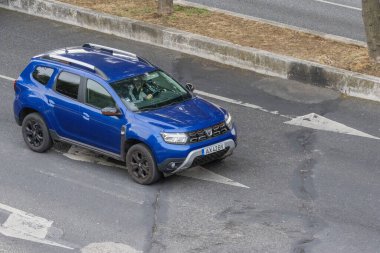 Mavi Dacia Tozcu SUV içinde bir şoförle caddede sürüyor.