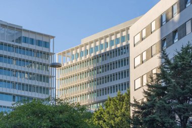 Gökyüzü altında cam cepheleri ve yeşil ağaçların bulunduğu modern ofis binaları