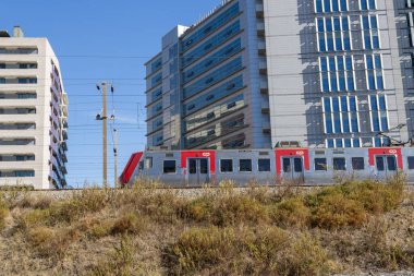 CP yolcu treni güneşli bir günde çağdaş mimari ve kuru bitki örtüsünü geçiyor