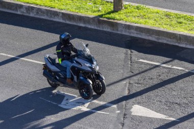 Üç tekerlekli bir Yamaha scooter kullanan bir sürücü her gün şehir yolunda gidip geliyor.