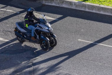 Yamaha üç tekerlekli scooterı güneşli bir günde şehir yolunda ilerliyor.