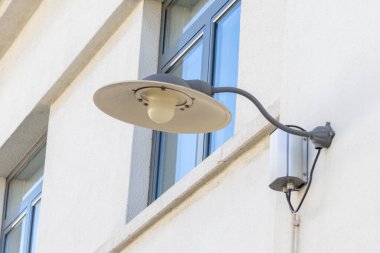 Dış duvarda modern bir sokak lambası ve mavi gökyüzünü yansıtan parlak bir pencere var.