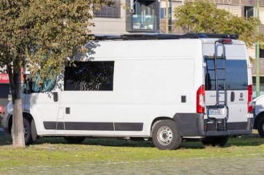 Beyaz Fiat Ducato karavanı. Merdiven ve güneş panelleri yeşil çimlere park edilmiş.