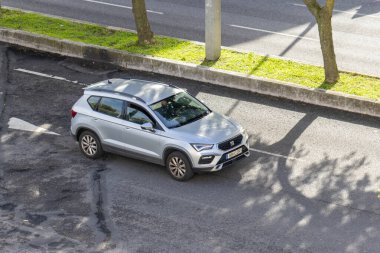 Gümüş koltuklu arazi aracı güneş ışığı ve ağaç gölgeleriyle bir şehir sokağında sürüyor.