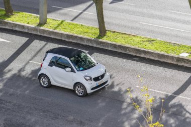 Asfalt caddesinde yeşil medyayla beyaz akıllı araba sürüyor.