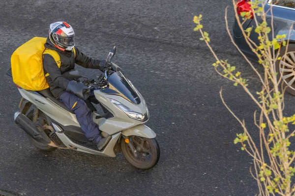 Asfalt yolda büyük sarı bir sırt çantasıyla motosikletli bir teslimatçı.