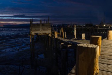 Alacakaranlıkta karrasqueira palafitik limanında geleneksel ahşap iskele alçak gelgit çamur düzlüklerini yansıtıyor.