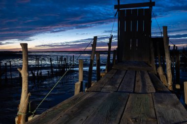 Eski ahşap iskele, alacakaranlıkta dalgalı gökyüzü ile suyun üzerinde ayakta duruyor.