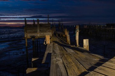Portekiz 'de günbatımında gelgit çamurunun üzerinde uzanan eski ahşap iskele.