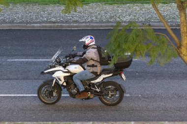 Biker wearing helmet and jacket riding benelli trk 502 motorcycle on a paved urban road