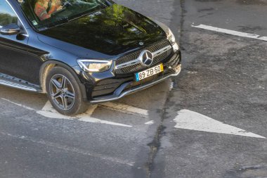 Siyah Mercedes Benz arabası, amblemli ve plakası asfalt yolda.
