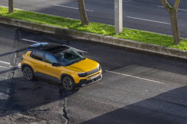 Sarı jip İntikamcısı asfalt yolda sabah ışığı altında, gölgeler bırakıyor.