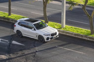 Kırık asfalt yolda yeşil çimenli beyaz BMW x5 SUV park yeri