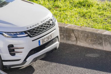 Beyaz Range Rover, yeşil çimenli, asfalt bir yola park etmiş.