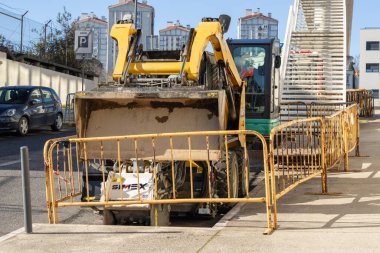 Kentsel kalkınma bölgesinde sarı güvenlik bariyerlerinin arkasında çalışan sıkıştırılmış fren motoru yükleyicisi