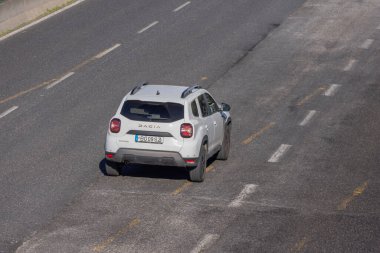 Beyaz Dacia Toz Bezi SUV asfalt yolda şerit işaretleriyle sürüyor.