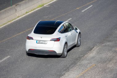 Beyaz Tesla modeli elektrikli cip güneşli bir günde asfalt bir otoyolda seyahat ediyor.