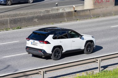 Beyaz toyota rav4 hibrit arazi aracı gün ışığında asfalt bir yolda ilerliyor.