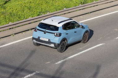 Yeşil bitki örtüsü ve güvenlik bariyeri olan asfalt yolda ilerleyen modern bir araba.