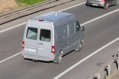 Gri teslimat minibüsü başka bir arabayla çok şeritli asfalt yolda gidiyor.