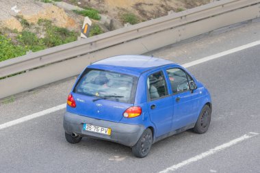 Mavi küçük hatchback araba asfalt yolda çarpışma bariyeriyle ilerliyor.
