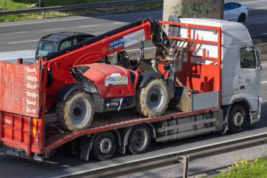 Kırmızı inşaat tele-idarecisi taşıyan bir kamyon otoban boyunca bir karavanda.
