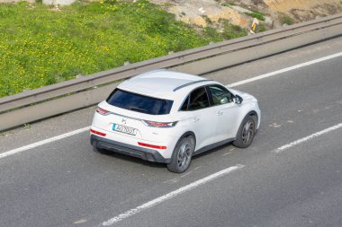 Yol kenarında yeşil çimenler olan asfalt bir yolda giden beyaz arazi aracı.