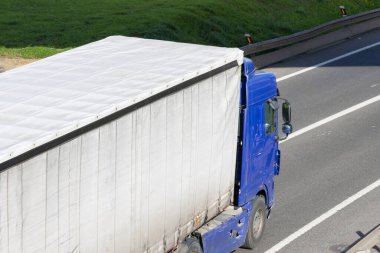 Mavi kamyonet, asfalt bir yolda, hava perspektifinden gidiyor.