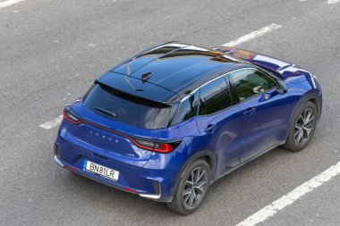 Mavi Lexus lbx kompakt SUv şehir manzaralı asfalt yolda gidiyor.