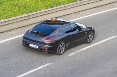 Porsche Panamera lüks arabası yeşil yol kenarlı asfalt bir otoyolda sürüyor.