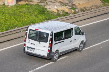 Beyaz minibüs, hava perspektifinden asfalt bir yolda mal taşıyor.