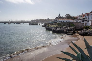 Kraliçe 'nin sahili, kumsalda dalgalar, kayalık kayalıklar ve uzak bir liman.