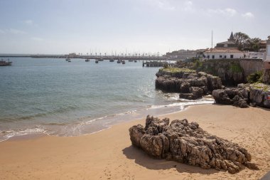Praia da Rainha 'nın güneşli manzarası, marinaya yakın kayalıkları ve okyanusu olan küçük bir plaj.