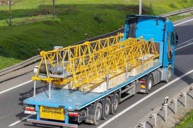 Düz bir karavanda parçalanmış sarı vinç parçaları ve beton kontra ağırlıklar taşıyan mavi kamyonet.