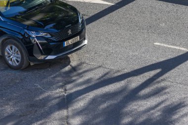 Siyah peugeot SUv gri asfalt bir yolda park etmiş, uzun, karanlık gölgeler döküyor.