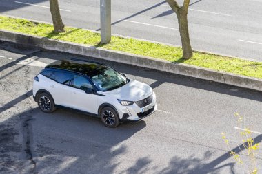 Beyaz peugeot 2008 SUV Ağaçlar ve çimlerle dolu bir şehir yolunda dönüyor