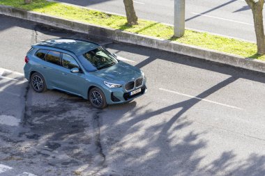 Bmw x1 ağaç gölgeleri ile güneş ışığı altında bir caddede yol alan kompakt SUv