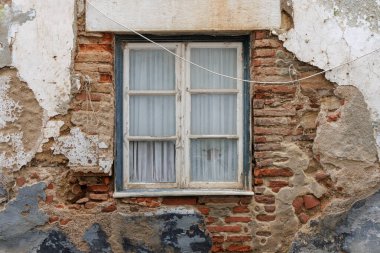 Eski bir binanın ön cephesindeki eski pencere alçı soyma ve açık tuğla işçiliğini gösteriyor