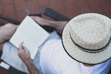 Şapkalı bir adam terasta kitap okuyor..