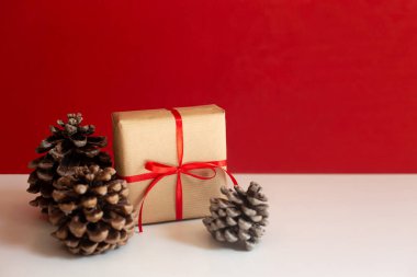 Kırmızı kurdeleli ve sedir kozalaklı kağıda sarılı yeni yıl hediyesi kırmızı arka planda..