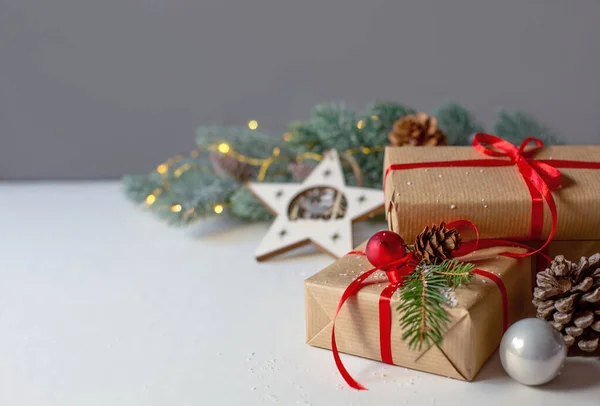 Kağıda sarılmış kırmızı kurdeleli Noel hediyeleri gri arka planda süslemeleri olan bir ladin dalının arka planında bulunuyor. Metin için boş alan.