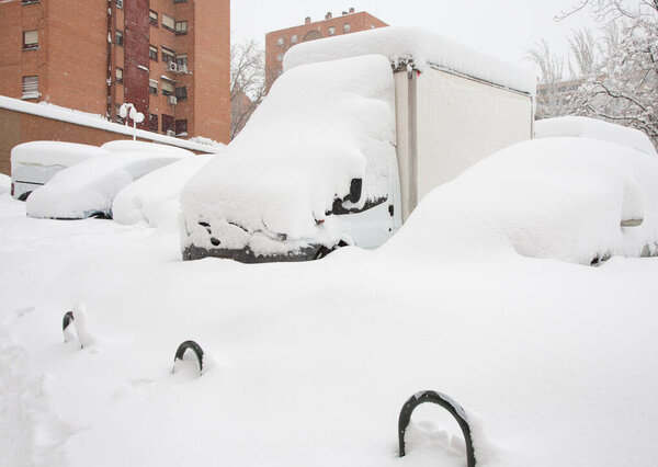 Cars completely covered with snow stand on a snowy street. Spain, January 2021.
