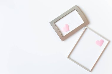 Resmin sağ tarafında pembe saten kalplerle süslenmiş iki gümüş fotoğraf çerçevesi var. Sevgililer Günü ya da düğün teması. Metin için boş alan.