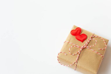 Kağıda sarılmış ve dekoratif kırmızı kalplerle süslenmiş bir hediye beyaz arka plandadır. Sevgililer Günü teması. Metin için boş alan.