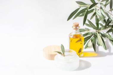 A glass jar with olive oil and olive tree twig are on white background. Natural cosmetics theme. Copy space.