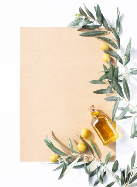 Beyaz arka planda boş bir kağıt ve zeytin yağı, zeytin ağacı filizi ve zeytin dolu cam bir şişe var. Sağlıklı yemek ve sağlıklı yaşam tarzı teması. Boşluğu kopyala.