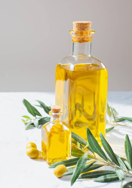 Стеклянные бутылки с оливковым маслом и оливковыми веточками и оливковыми деревьями находятся на сером фоне. Тема здорового питания.