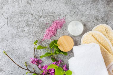 Spa seti. Krem, banyo terlikleri ve beyaz havlu gri arka planda. Boşluğu kopyala.